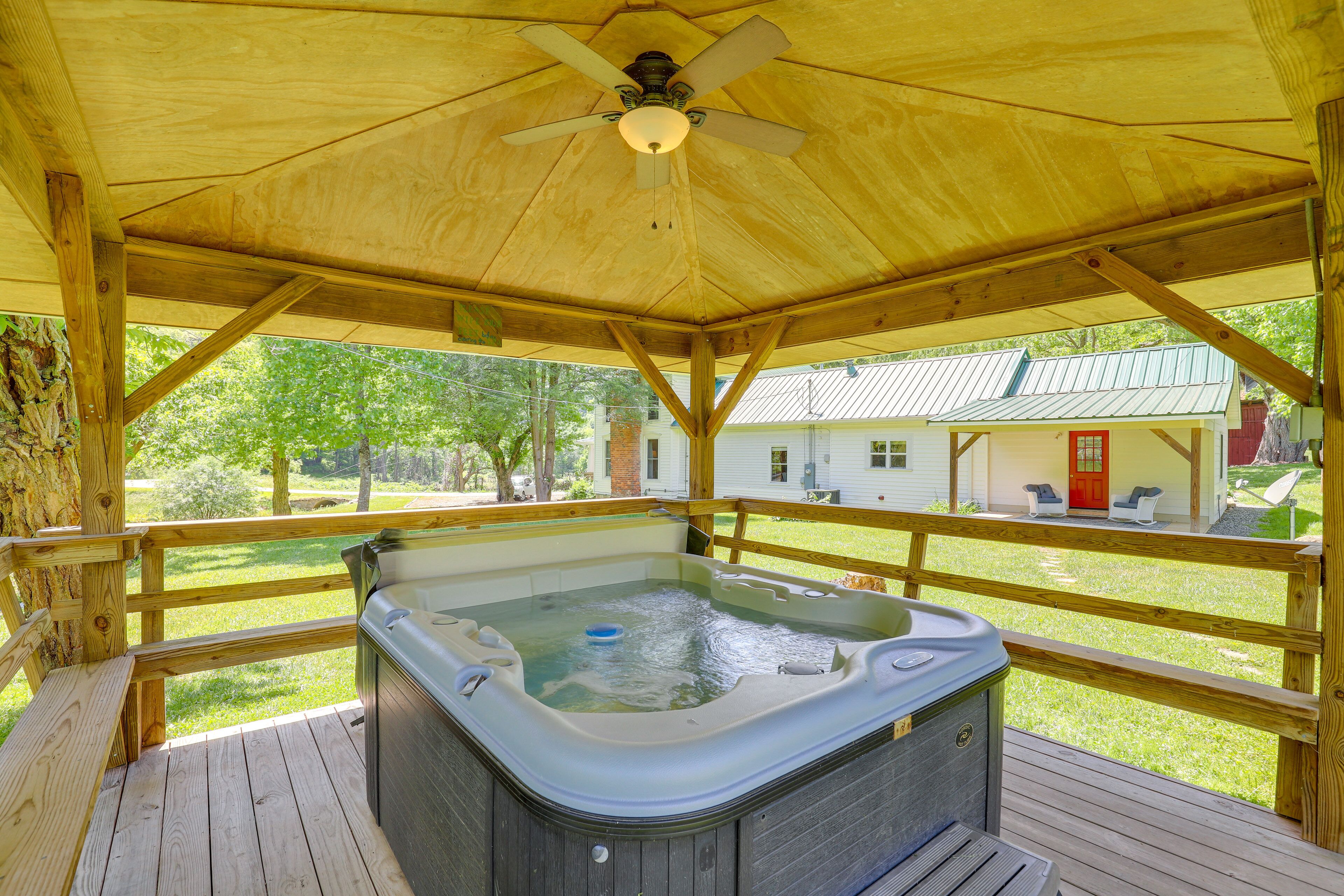 Une terrasse en bois avec un jacuzzi, un ventilateur de plafond et une vue sur une maison en arrière-plan.