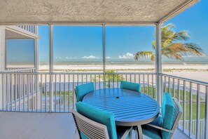 A balcony with a view of the beach, a round table with chairs, and a railing.