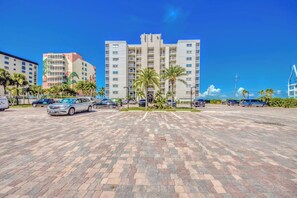 A parking lot with multiple cars, a large building with balconies, and palm trees.