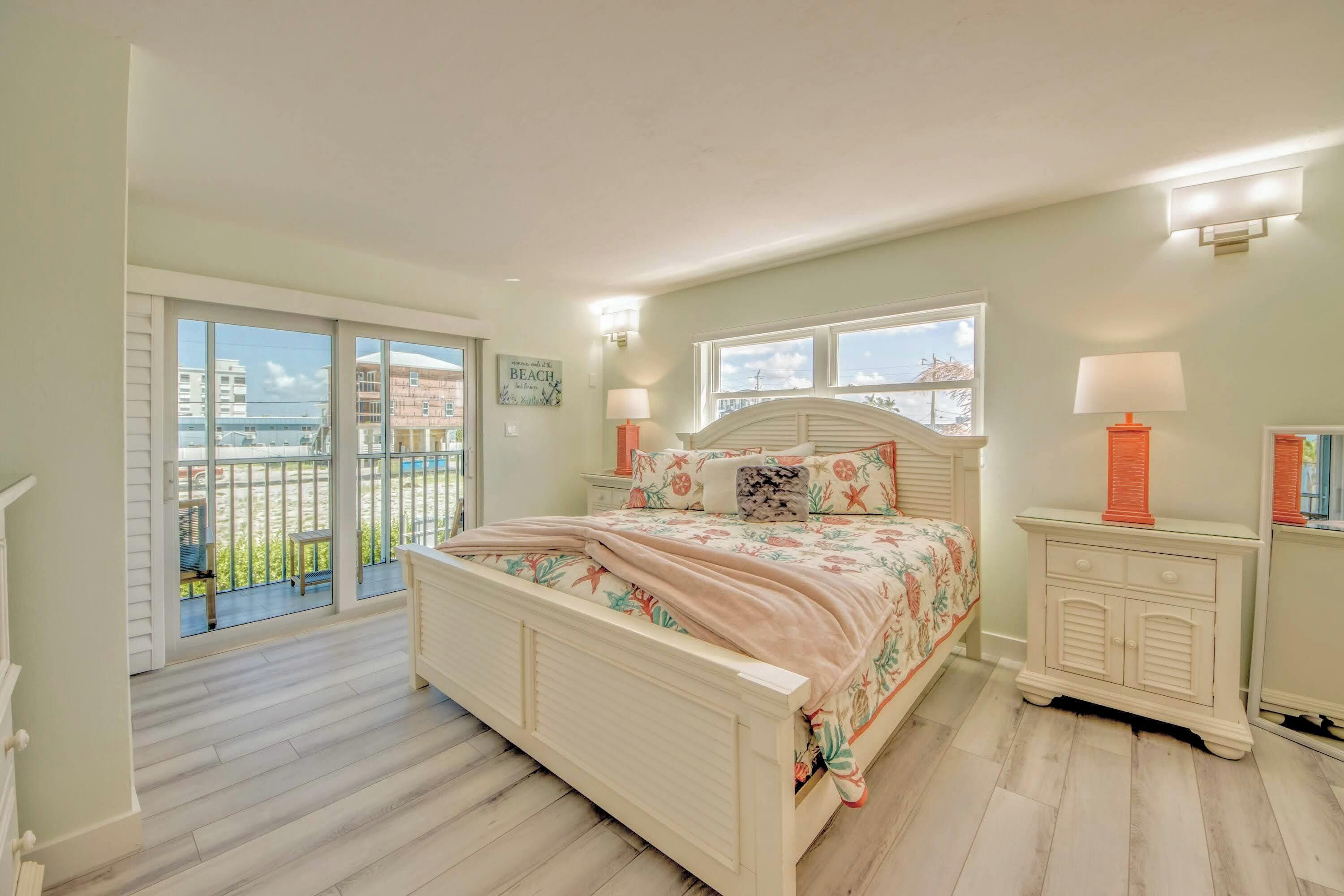 A bedroom with a large bed, a nightstand, a dresser, and a view of the outside.