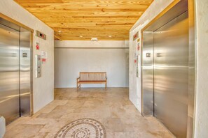 An elevator area with two elevators, a wooden bench, and a patterned floor.