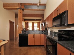 A kitchen with wooden cabinets, a black stove, and a microwave. - Historic Loft w/ Exposed Brick & Timber Beams (Victoria, B.C.)