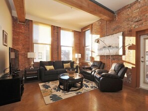 A living room with a brick wall, a fireplace, a sofa, a coffee table, and a television.