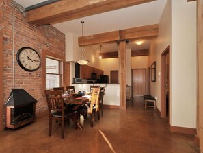 A dining area with a brick wall, a clock, and a fireplace. - Historic Loft w/ Exposed Brick & Timber Beams (Victoria, B.C.)