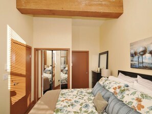 A bedroom with a bed, a nightstand, a lamp, a painting, and a door leading to another room.