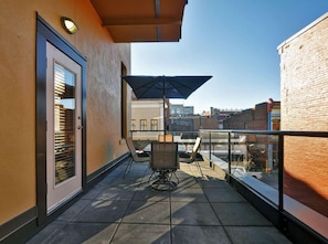 A balcony with a table and chairs, a door with blinds, and a view of the cityscape. - Historic Loft w/ Exposed Brick & Timber Beams (Victoria, B.C.)