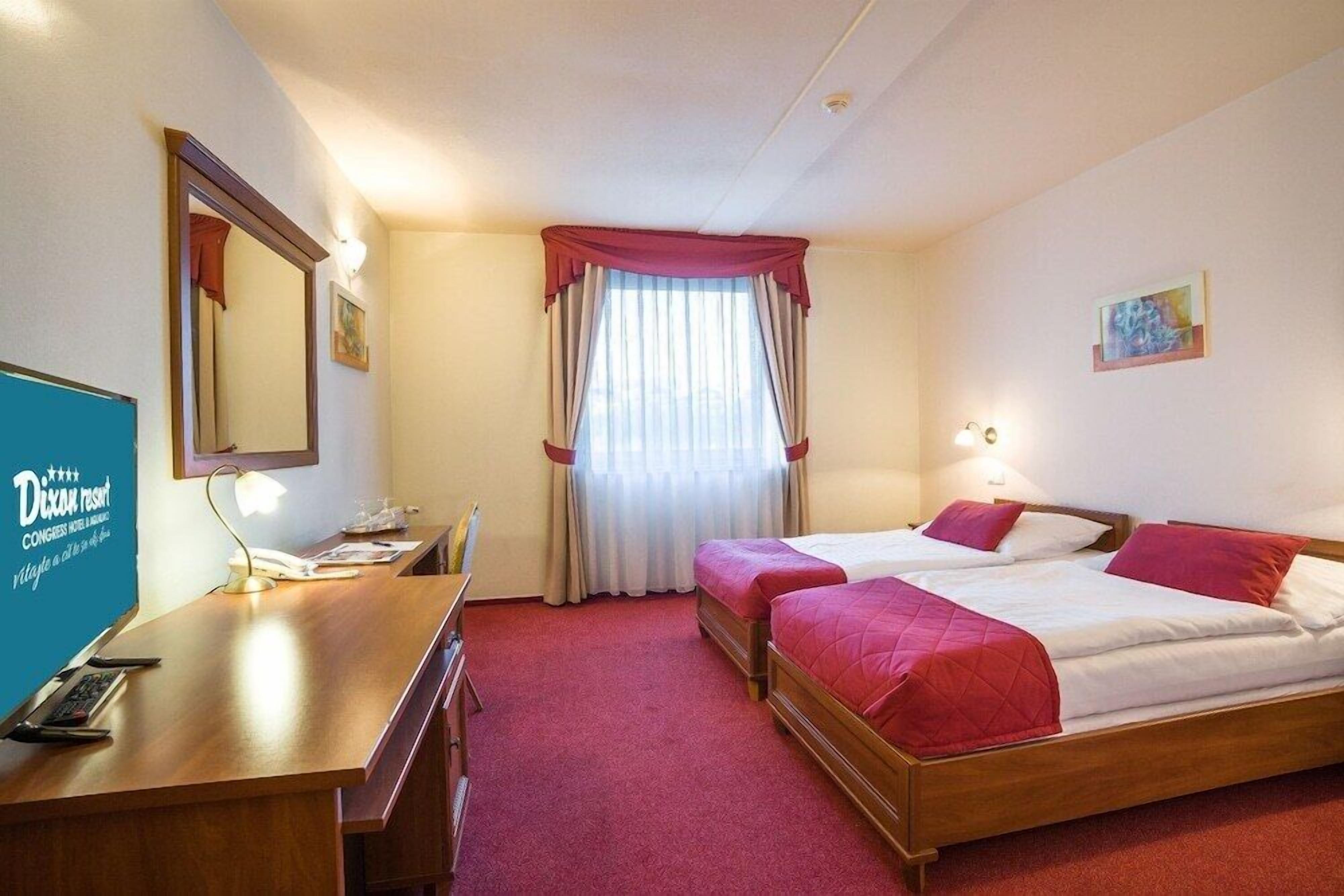A hotel room with two beds, a desk with a telephone, and a mirror.