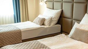 Habitación de hotel con dos camas, cada una con cubrecama acolchado y almohadas, cabecero acolchado y lámpara fijada a la pared.