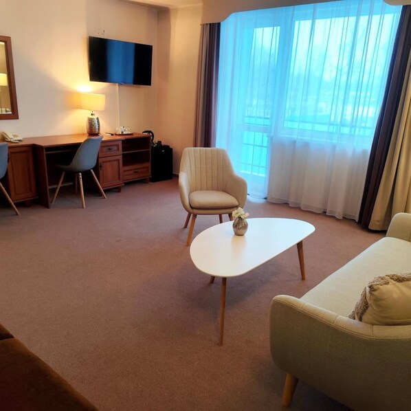 A hotel room with a desk, chair, sofa, TV, and large windows.