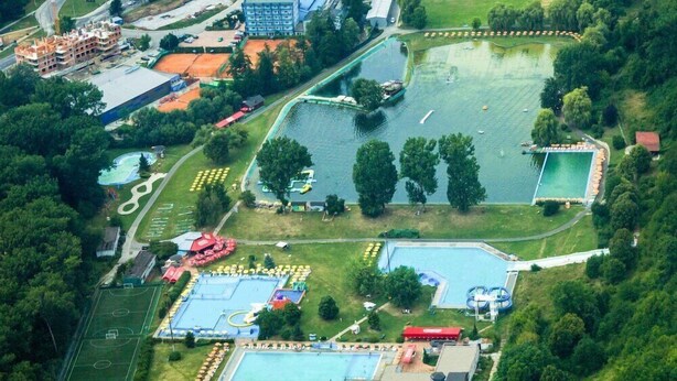Vista aérea de un área recreativa con varias piscinas, un campo deportivo y zonas verdes circundantes.