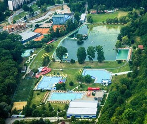 An aerial view of a recreational area with multiple swimming pools, a sports field, and surrounding greenery.