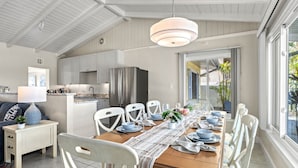Una cocina moderna con armarios blancos, un refrigerador de acero inoxidable y una zona de comedor con una mesa de madera preparada para seis comensales.