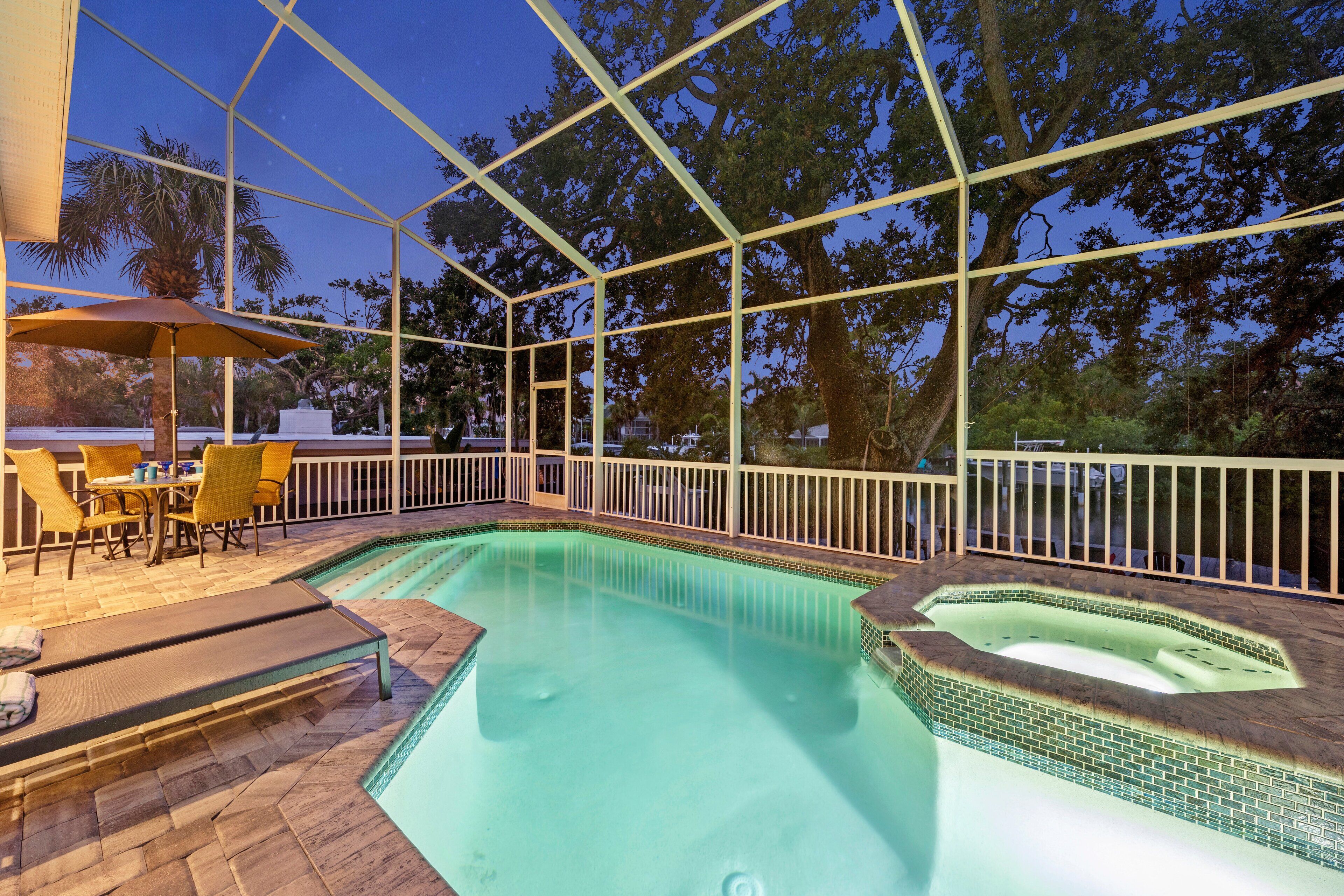 A swimming pool with a sunken hot tub, surrounded by a covered patio with chairs and an umbrella.