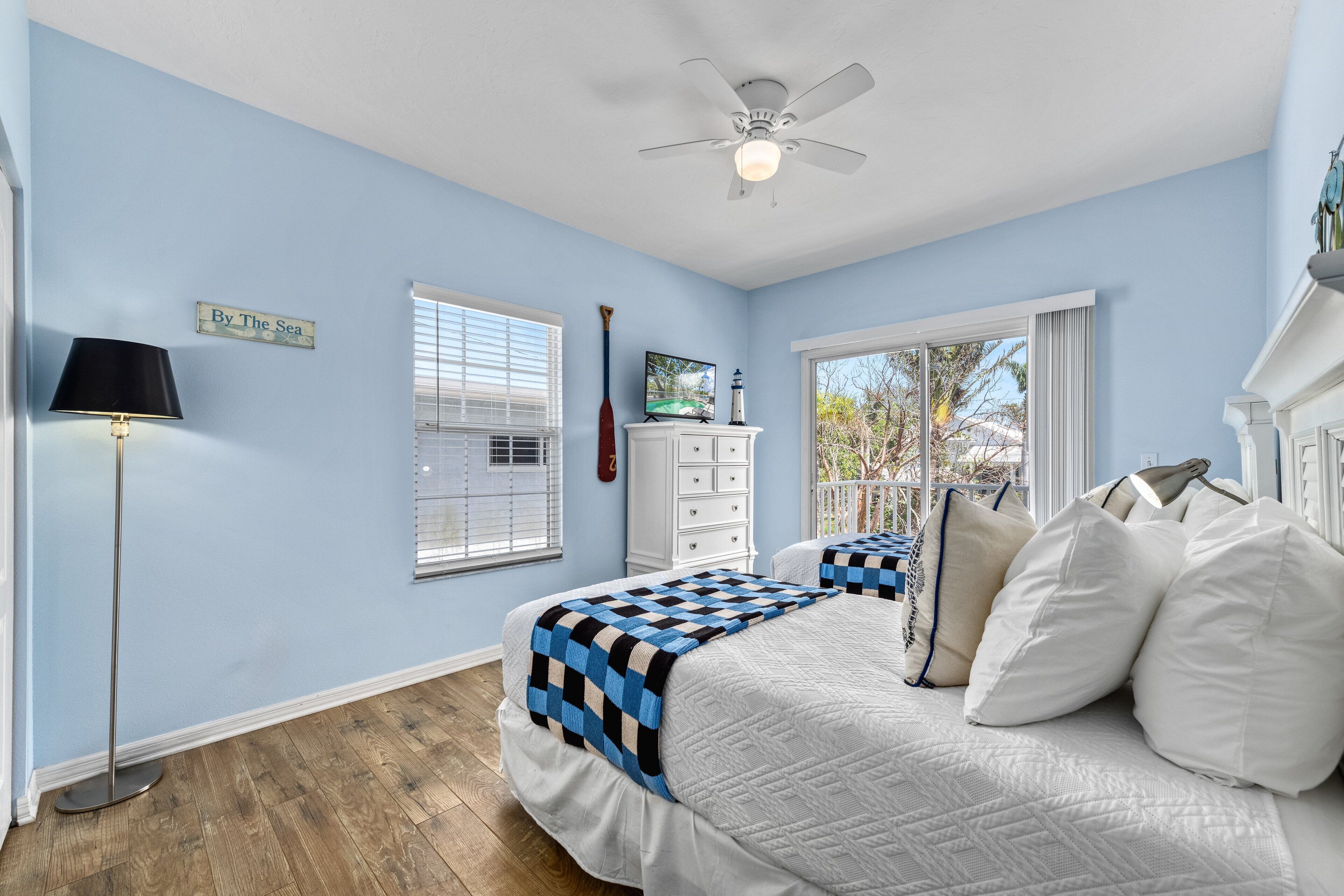 A bedroom with two beds, a ceiling fan, a window with blinds, a lamp, and a sign on the wall.
