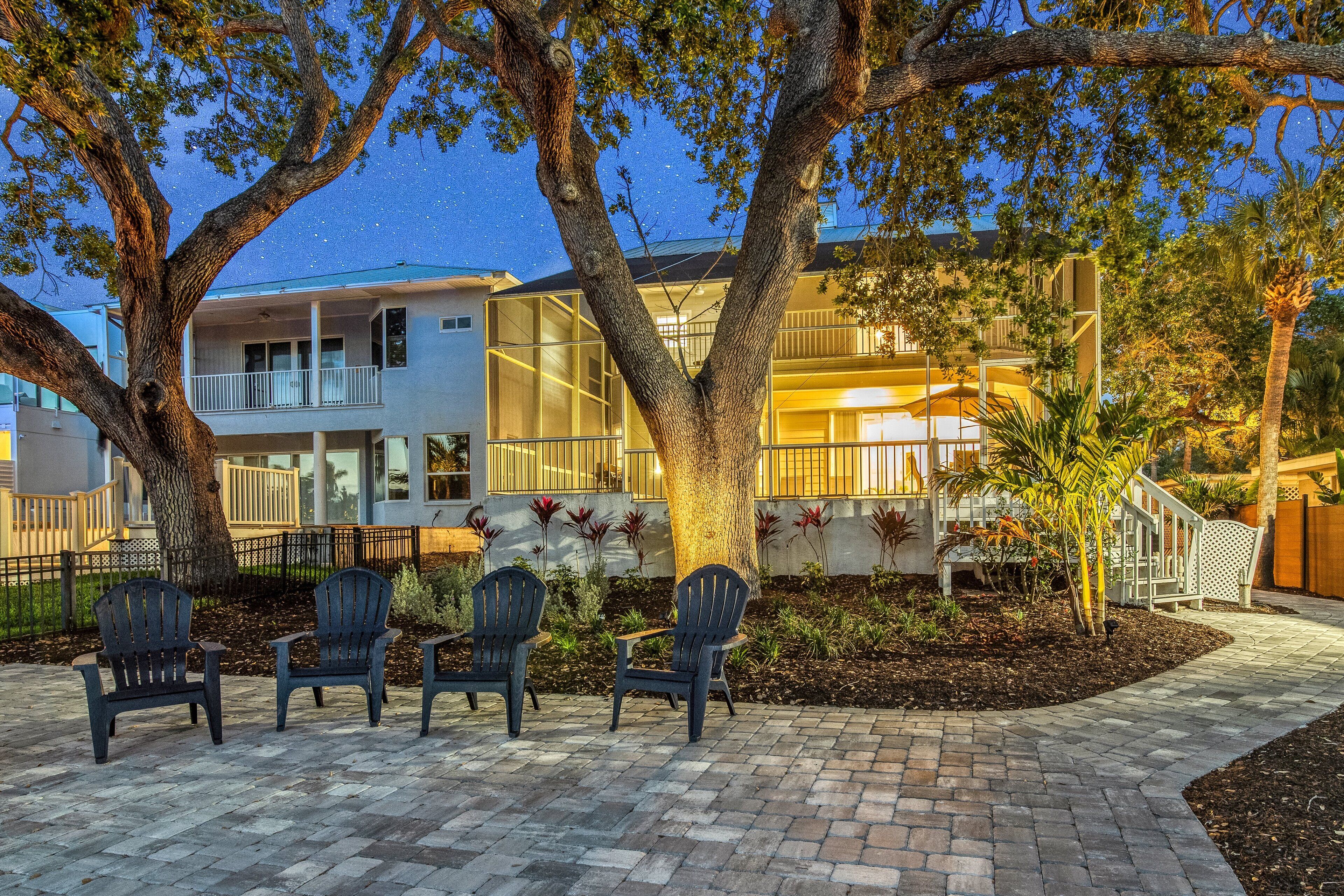 A modern house with a balcony, a paved patio with chairs, and a well-maintained garden.