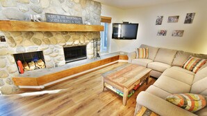 A cozy living room with a stone fireplace, a flat-screen TV, and a sectional sofa. - On River, Pool, 2 Hot Tubs! Walk to Main St Dining, Shops, Events (Frisco)