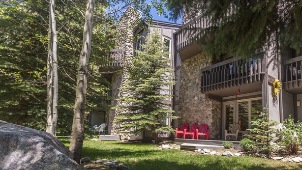 A modern building with a stone facade, a balcony with railings, and a small garden area with red chairs. - On River, Pool, 2 Hot Tubs! Walk to Main St Dining, Shops, Events (Frisco)