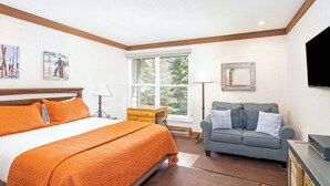 A bedroom with a large bed, a sofa, a TV, and artwork on the walls. - Updated Hotel Room With Kitchenette at the Mountainside Inn (Telluride)