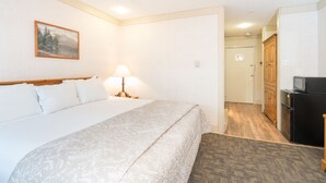 A hotel room with a bed, a lamp, a painting on the wall, and a kitchen area with cabinets and a refrigerator. - Upgraded Floors and King Bed at Mountainside Inn (Telluride)