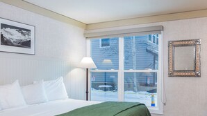 A hotel room with a bed, a window with a view of the outside, a framed picture on the wall, and a decorative mirror.