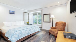 Quarto de hotel com cama, poltrona, mesa, abajur e televisão.