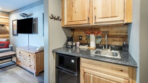 A compact kitchen with wooden cabinets, a built-in dishwasher, a coffee maker, and a flat-screen TV mounted on the wall. - Riverside Hotel Room With Split-King Bed (Telluride)