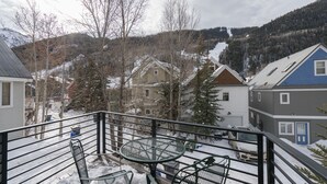 Un balcone con tavolo e sedie, affacciato su una zona residenziale innevata con case e alberi.