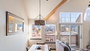 A cozy living room with a dining area, large windows offering scenic mountain views, and a wooden ceiling beam. - Near Lake Trail! Hot Tub! Walk to Dining, Shops, Brewpub, Bike Rental (Frisco)