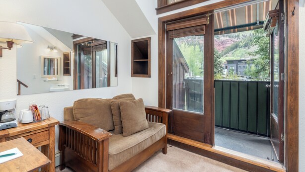 A room with a wooden sofa, a desk with a coffee maker, a mirror, and a large window with a view of a building and trees. - Get An Authentic Telluride Experience in This Classic Ski Chalet Room (Telluride)