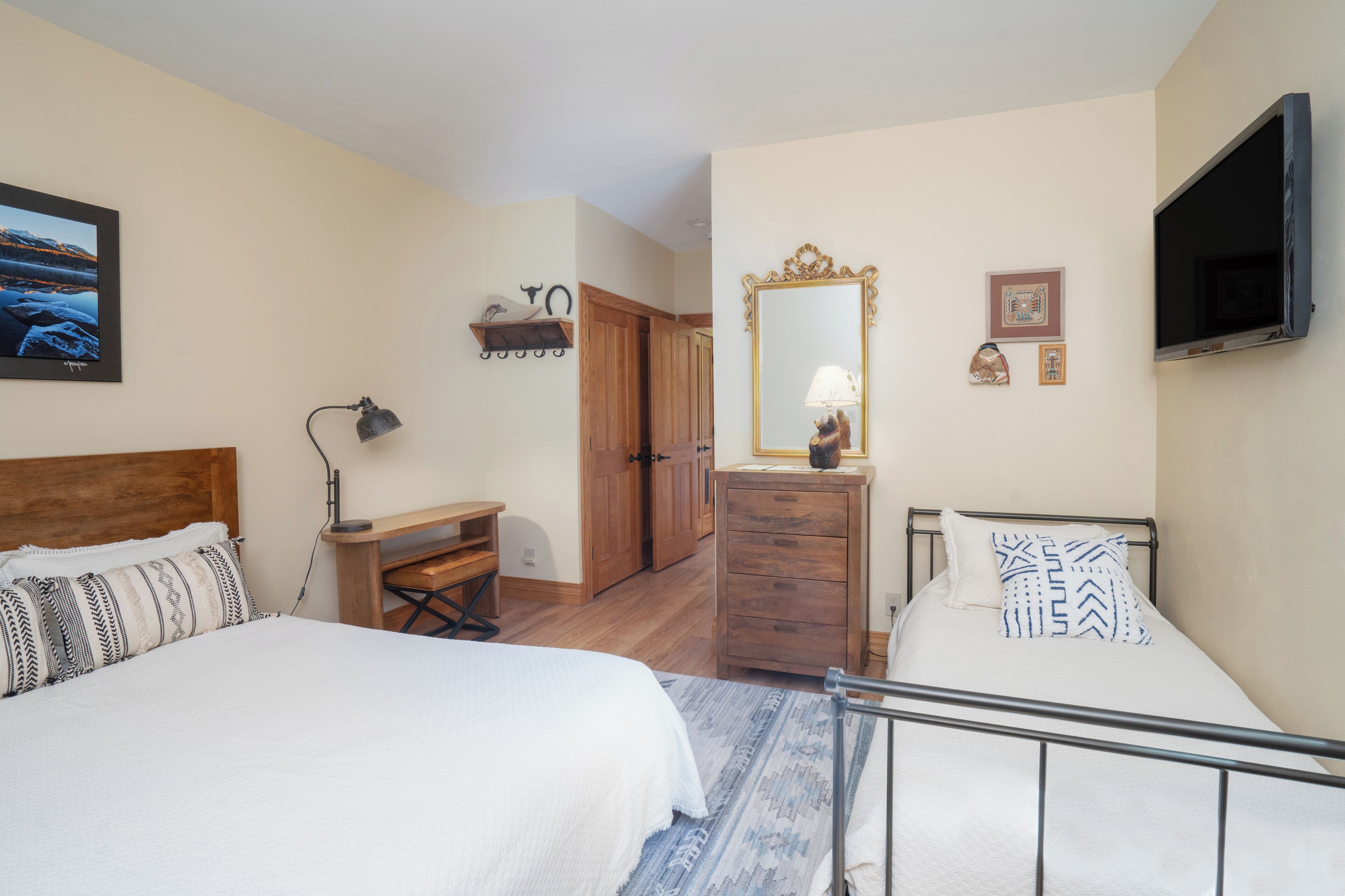 A bedroom with two beds, a desk, a dresser, a mirror, and a TV.