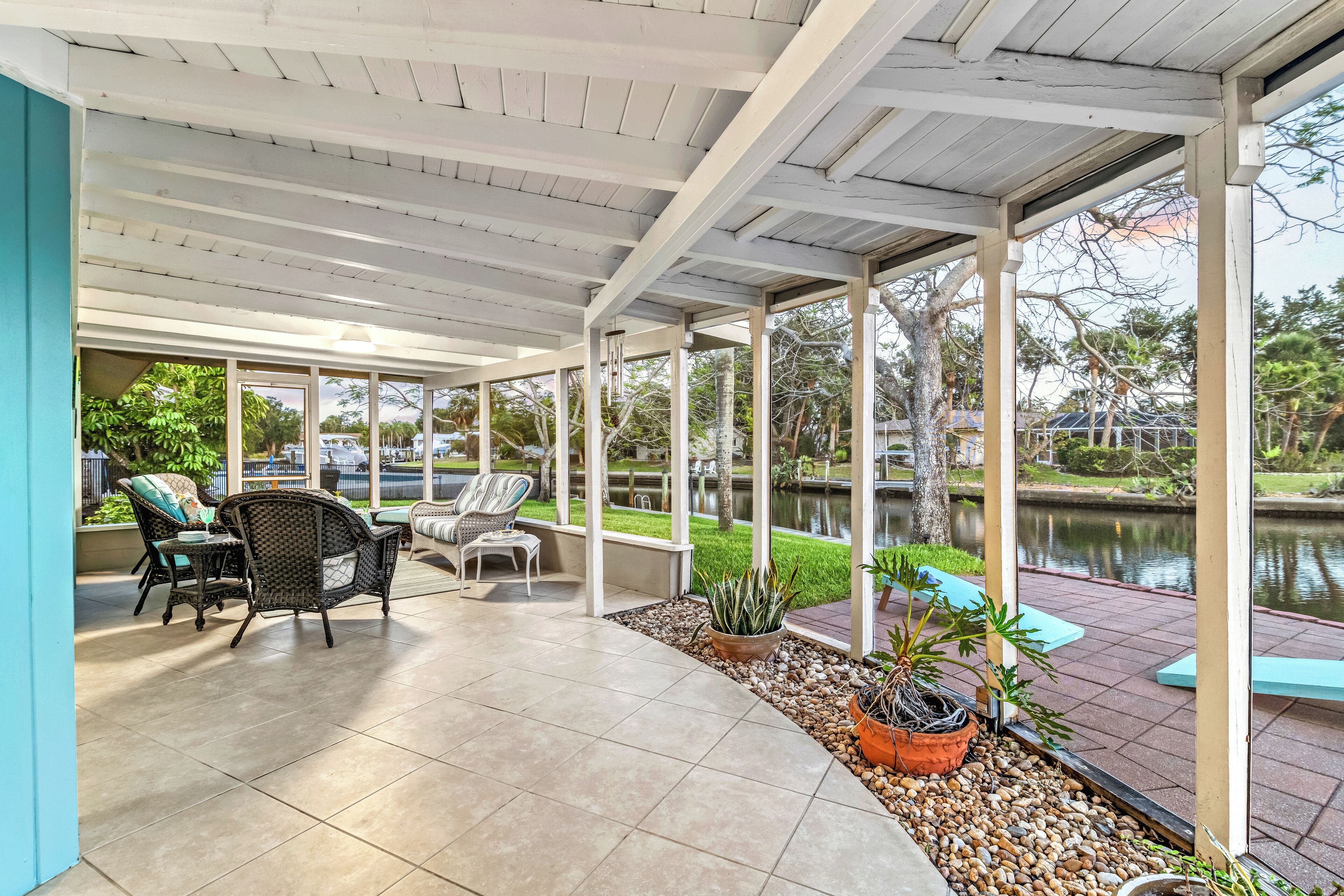 A covered patio area with wicker furniture, potted plants, and a view of a body of water.