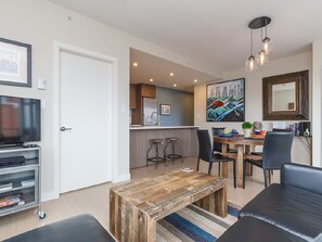A modern living room with a wooden coffee table, black leather sofa, and a TV. - Bright Open-Concept Sanctuary at The Era (Victoria)