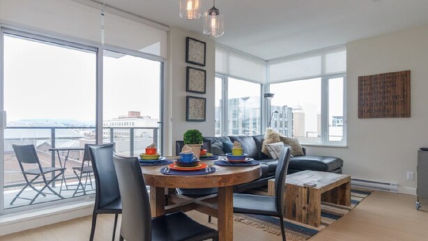 Een moderne woonkamer met een eethoek, grote ramen en uitzicht op de stad.