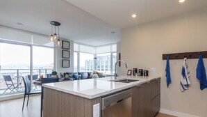 Een moderne keuken met een centraal eiland, een zithoek met een bank en stoelen, en een stadszicht door grote ramen.
