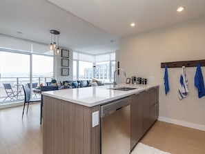 A modern kitchen with a central island, a dining area with a sofa and chairs, and a view of the city through large windows. - Bright Open-Concept Sanctuary at The Era (Victoria)