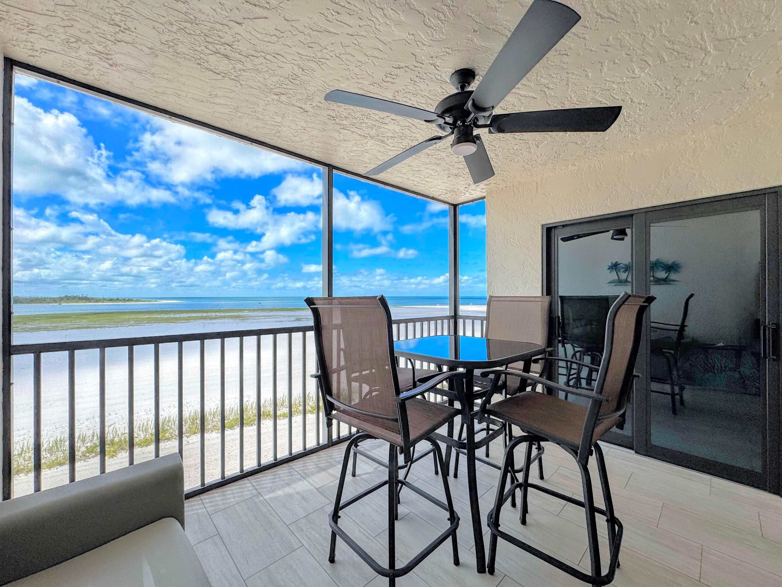 A balcony with a table and chairs, a ceiling fan, and a view of the beach.