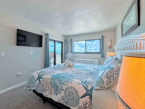 A bedroom with a bed, a nightstand, a lamp, a window, and a view of the outdoors. - Carlos Pointe #335 Cute Beachfront Condo (Fort Myers Beach)