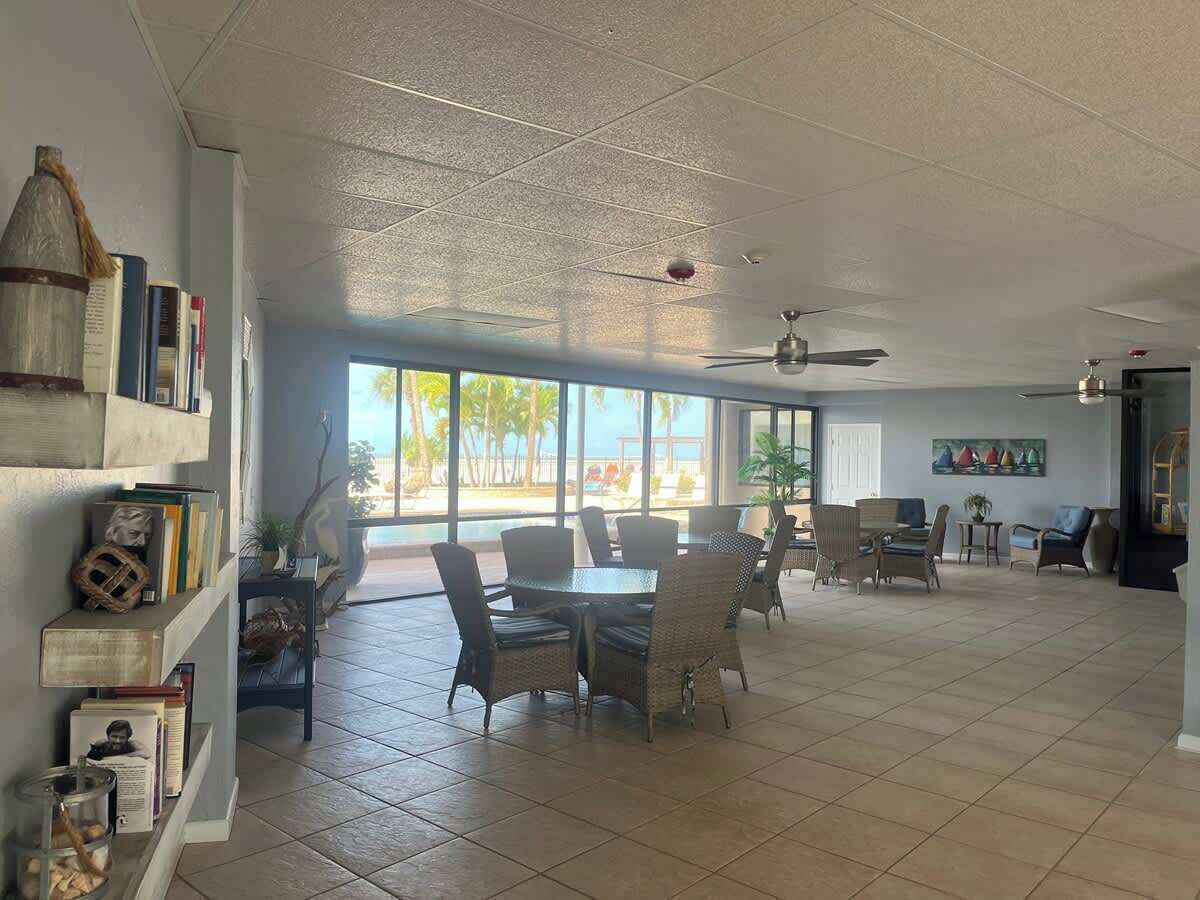 A spacious room with a dining area, large windows, and a ceiling fan.