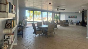 A spacious room with a dining area, large windows, and a ceiling fan. - Carlos Pointe #335 Cute Beachfront Condo (Fort Myers Beach)