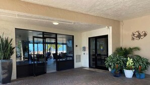 A covered outdoor area with brick flooring, glass doors leading to an interior space, and potted plants. - Carlos Pointe #335 Cute Beachfront Condo (Fort Myers Beach)