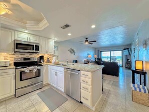 A modern kitchen with stainless steel appliances, a central island, and a dining area with a view. - Carlos Pointe #335 Cute Beachfront Condo (Fort Myers Beach)