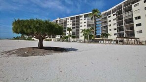 A multi-story hotel with balconies, a sandy beach in front, and palm trees. - Carlos Pointe #335 Cute Beachfront Condo (Fort Myers Beach)