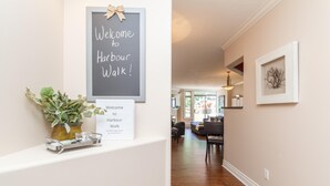 A hallway with a welcome sign, a framed welcome sign, a potted plant, and a framed artwork on the wall.