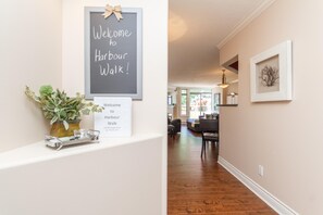 A hallway with a welcome sign, a framed welcome sign, a potted plant, and a framed artwork on the wall. - Versatile Garden-Level Suite w/ Natural Light (Victoria)
