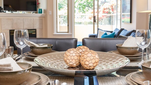 A dining table set with plates, bowls, and glasses, with a view of a garden through a large window.