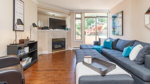 A living room with a grey sectional sofa, a fireplace, a flat-screen TV, and a bookshelf.