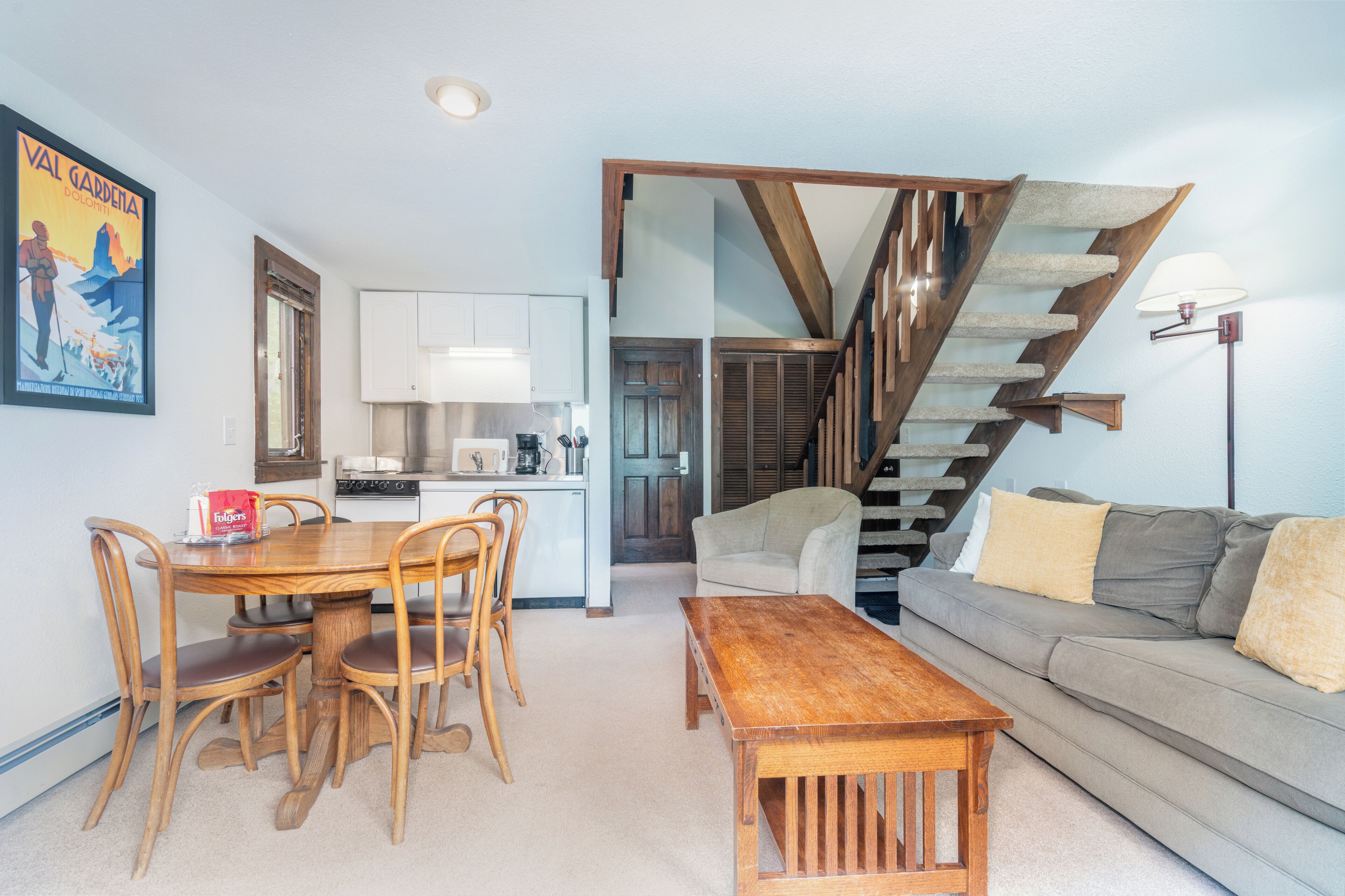 Een eetgedeelte met een houten tafel en stoelen, een bank, een trap en een keuken op de achtergrond.