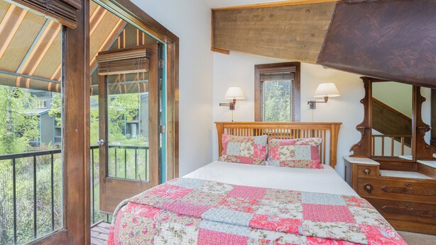 A bedroom with a large bed, wooden headboard, two wall-mounted lamps, a mirror, and a wooden dresser. - Sleep Six in This Private Lofted Room With a Kitchenette (Telluride)