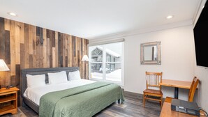 Ein Schlafzimmer mit Bett, Holzwandverkleidung, einem Fenster mit Blick, einem Sessel, einem Tisch und einem Spiegel.