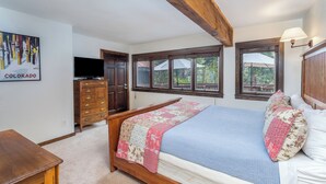Ein Schlafzimmer mit einem Bett, einem Holzschrank, einem Fernseher und Fenstern.